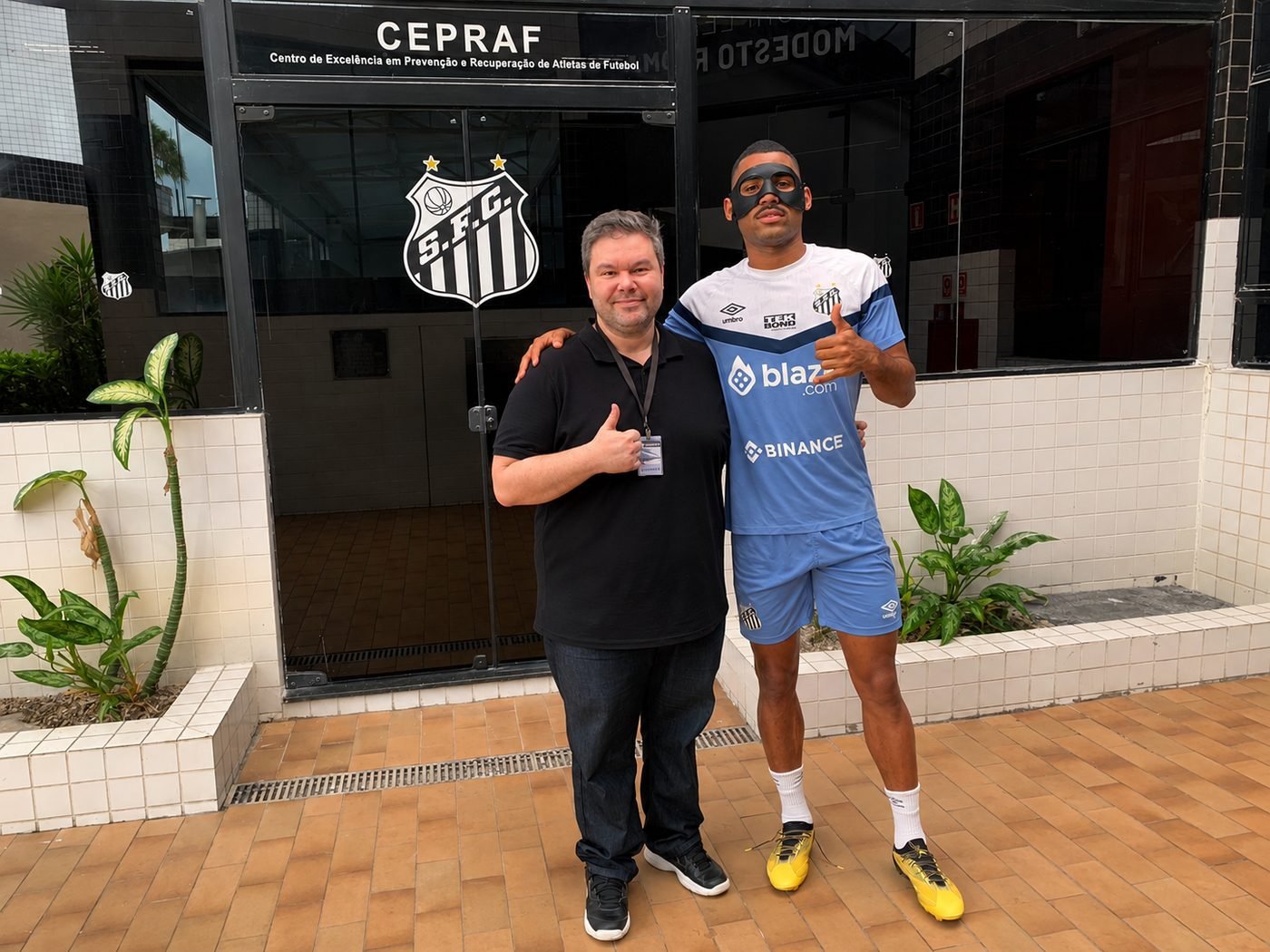 Dr. Caio Capitani ao lado de atleta do Santos FC com máscara de proteção facial, em frente ao CEPRAF do Santos Futebol Clube